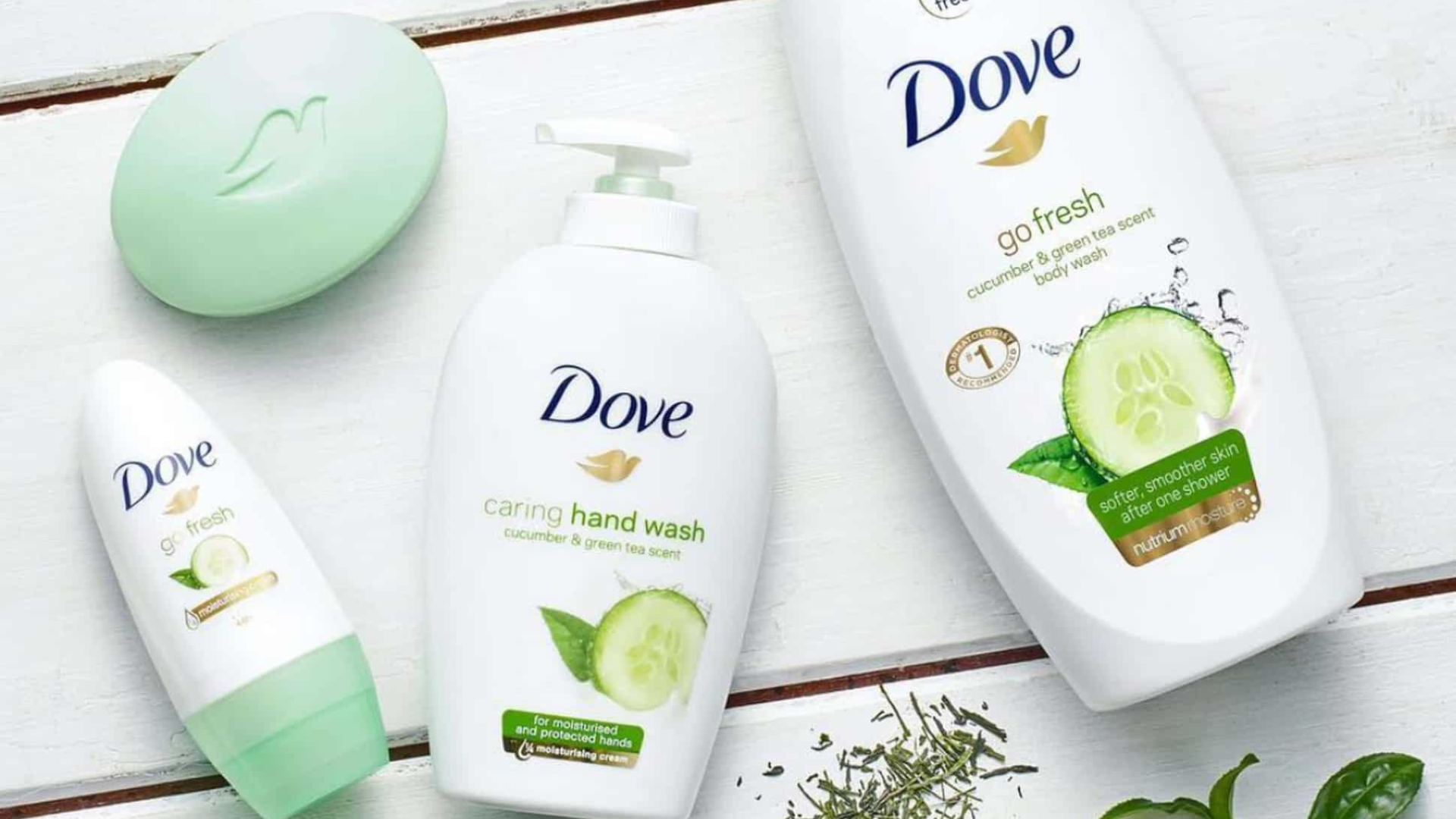 3 bottles of Dove product and a lime green bar soap laying flat on a white wooden floor