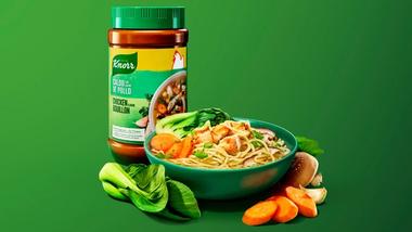 Jar of Knorr Chicken Bouillon next to a bowl of noodles with vegetables.