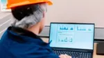 Factory worker in hard hat and navy-blue overalls facing a computer screen displaying data and H2Ok Innovation’s company logo