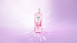 Pink LUX Bright pump bottle featuring a magnolia flower design, centred against a soft pink and lilac background with radiant, light reflections.