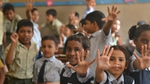 Children in a classroom raise their hands and smile at the camera, having taken part in a Lifebuoy handwashing lesson