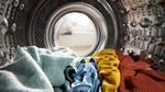Close-up view from inside a washing machine drum, showing laundry in shades of green, blue, yellow and red ready to be washed.