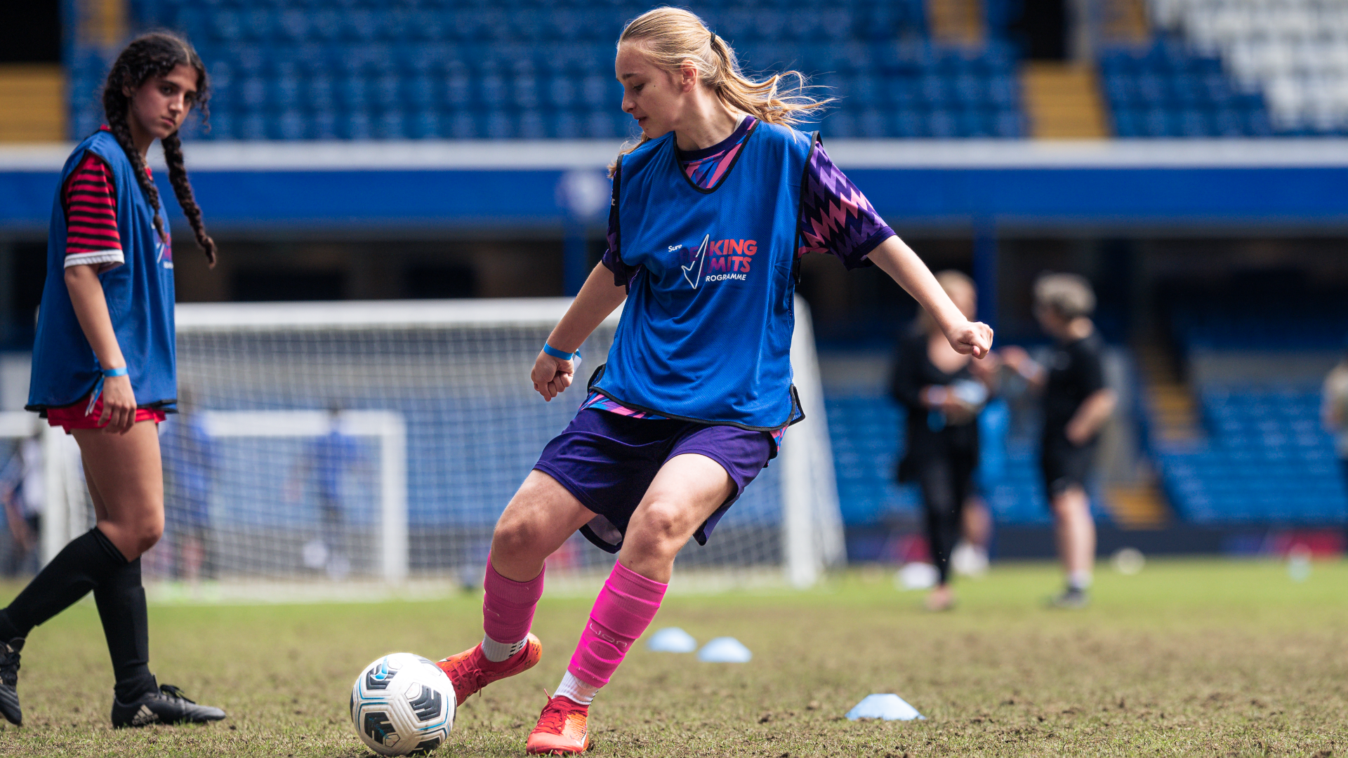 A blonde young woman playing football in a blue kit. Rexona's Breaking Limits Program in action at Chelsea.