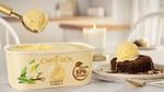 Tub of vanilla Carte D’Or ice cream on table and scoop on top of chocolate dessert.