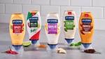 A display of Hellmann’s flavoured mayonnaise on a counter top. Flavours from left to right include: Spicy, Chilli Lime, Garlic Aioli, Italian Herb & Garlic, Chipotle.