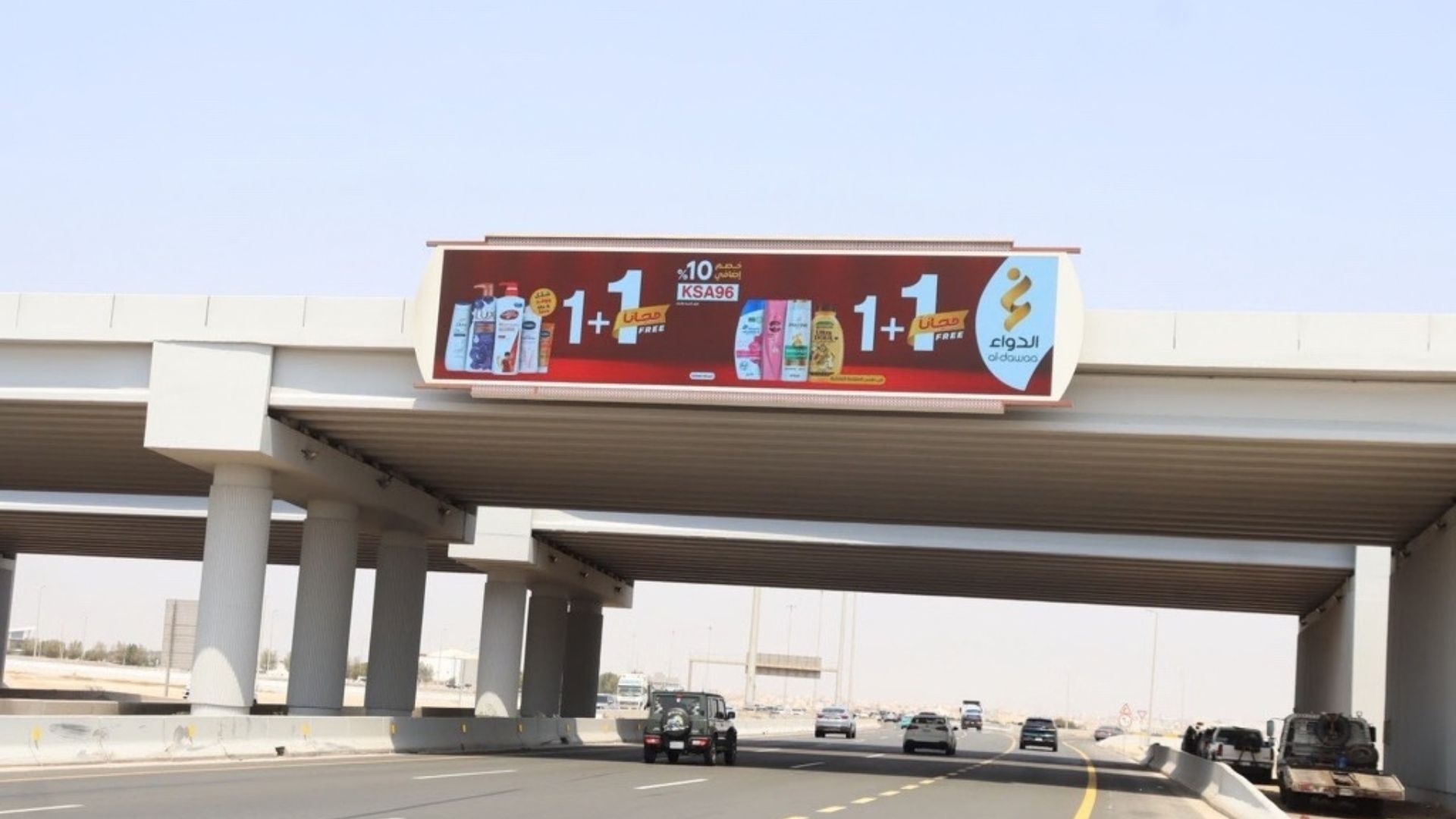 Al-Dawaa pharmacy billboard advertises a buy-one-get-one-free offer above a multilane highway.