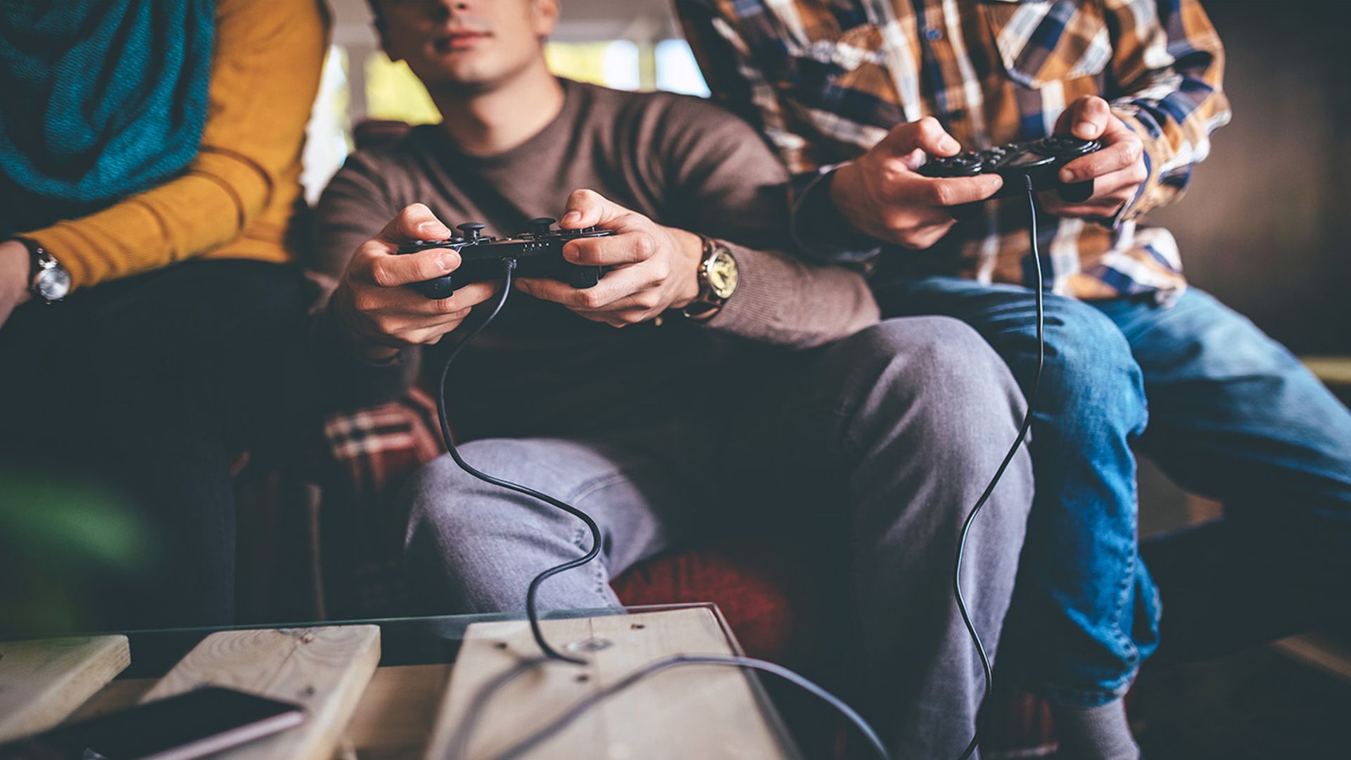 Photo focused in on the hands of three people sitting on a sofa using games consoles to play an online game